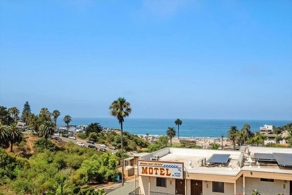 View of the ocean and shoreline from an elevated position, with trees and a motel building in the foreground.
