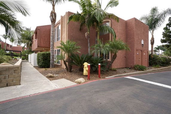 Front view of a multi-story building with a stucco exterior and various plants around it.