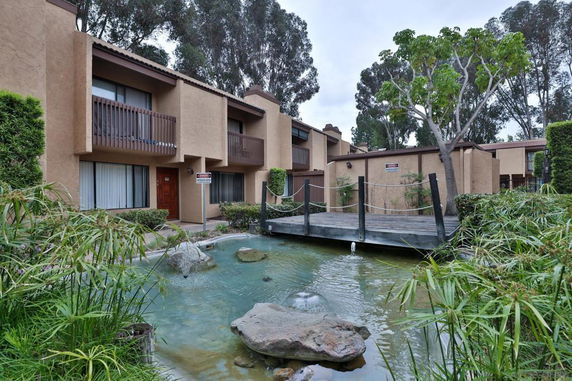 Front view of a multi-story apartment building with balconies and a water feature in front.