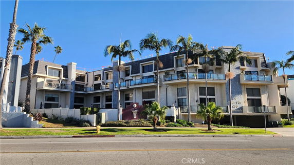 Front view of a multi-story building with balconies and palm trees.