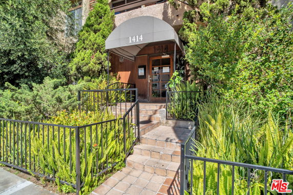Front view of a building entrance with stairs and greenery.