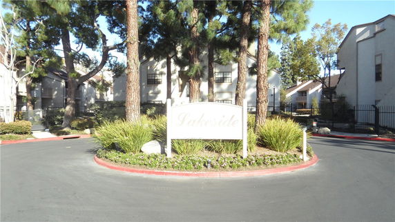 Front view of residential buildings with a sign reading 'Lakeside' and surrounded by trees and fencing.