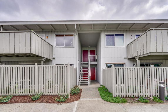 Front view of a two-story building with balconies and a red door entrance.