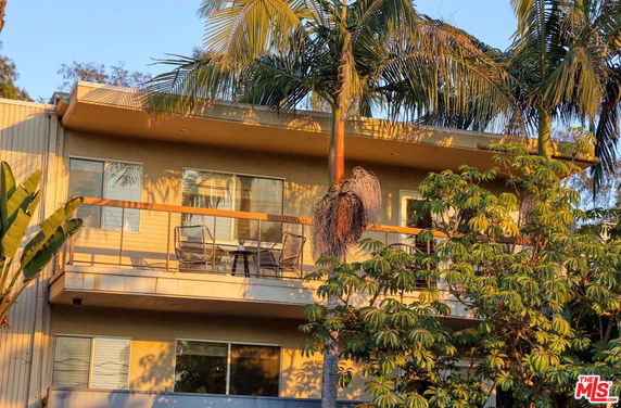 Front view of a two-story building with balconies and palm trees.