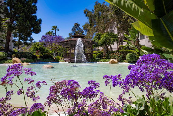 Outdoor area with a pond, fountain, gazebo, and surrounding greenery.
