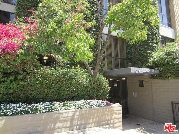 Front view of an apartment building entrance with greenery and flowers.