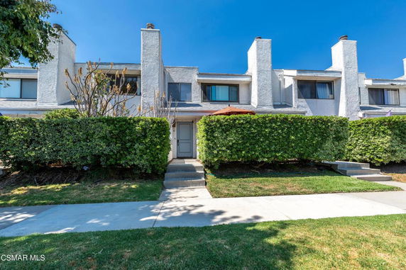 Front view of a two-story townhouse with white exterior and hedges.