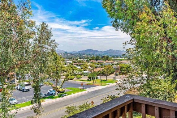 View of a neighborhood and distant hills from a balcony, surrounded by trees.