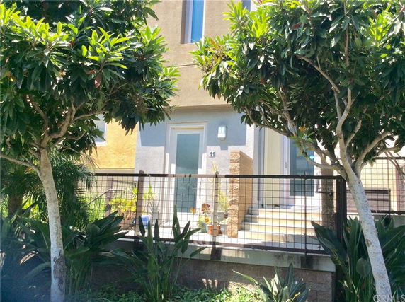 Front view of a house with stairs leading to the entrance, surrounded by trees and plants.