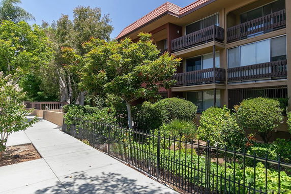 Front view of a multi-story residential building with balconies and a landscaped garden.