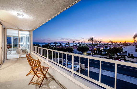 Panoramic view from a balcony overlooking a street and distant ocean at sunset.