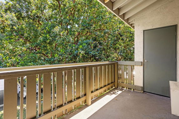 Outdoor balcony area with a railing and a door, surrounded by trees.