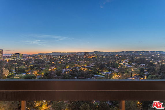 Panoramic view of a cityscape at dusk with buildings and mountains in the distance.