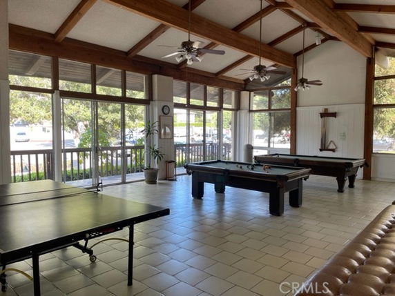 Room with pool tables, table tennis, and seating, featuring large windows and ceiling fans.