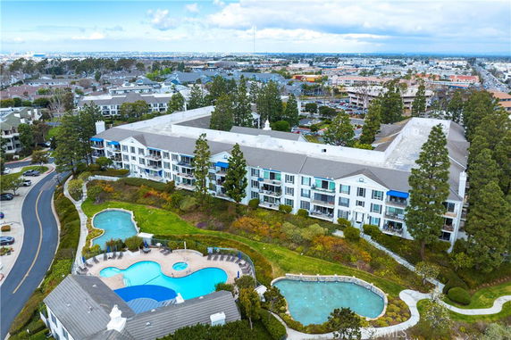 Aerial view of a multi-story residential building with surrounding landscape and swimming pools.
