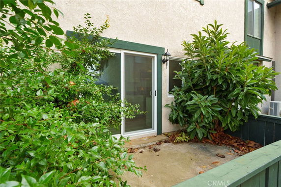 Exterior view of a building with a sliding glass door and green trim, surrounded by plants.