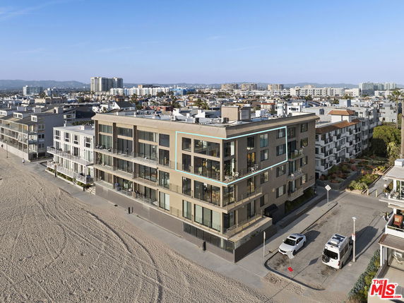 Front view of a large, modern multi-story beachfront building with glass balconies.