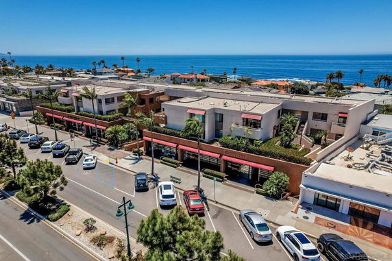 Aerial view of a commercial area near the ocean with multiple cars parked on the street and ocean in the background.