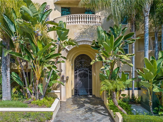 Front view of a house with a decorative iron gate and arched entrance surrounded by tropical plants.
