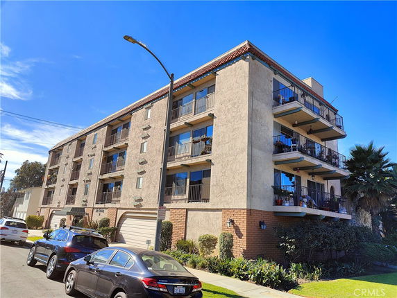 Front view of a multi-story apartment building with balconies and a sloped roof.