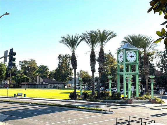View of a park area with a prominent clock tower and palm trees, adjacent to a street with a traffic light.
