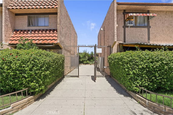 Front view of two connected buildings with gated entrance and hedges on either side.