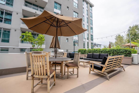 Rooftop sitting area with table, chairs, and umbrella, adjacent to a multi-story building.