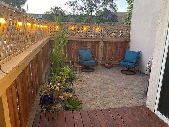 Outdoor patio area with wooden fencing, string lights, plants, and blue cushioned chairs.