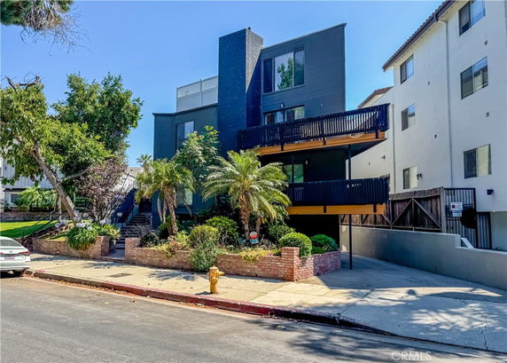 Front view of a modern multi-story building with balconies and surrounding greenery.