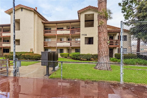 Front view of a multi-story building with balconies and a fence.