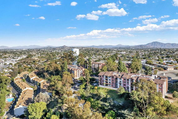 Aerial view showing buildings surrounded by trees with a cityscape and mountains in the background.