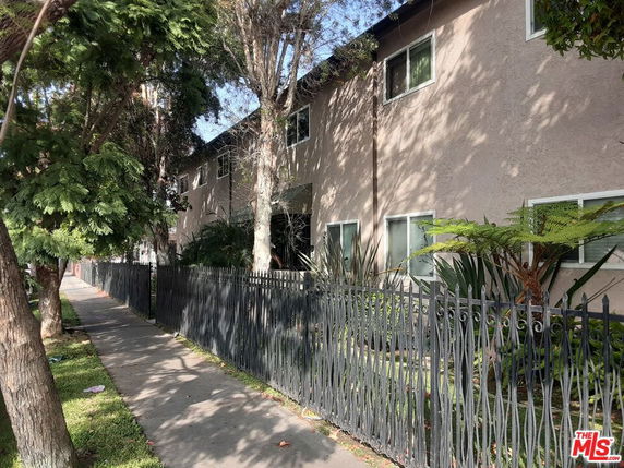 Side view of a multi-story residential building with a fence and trees.