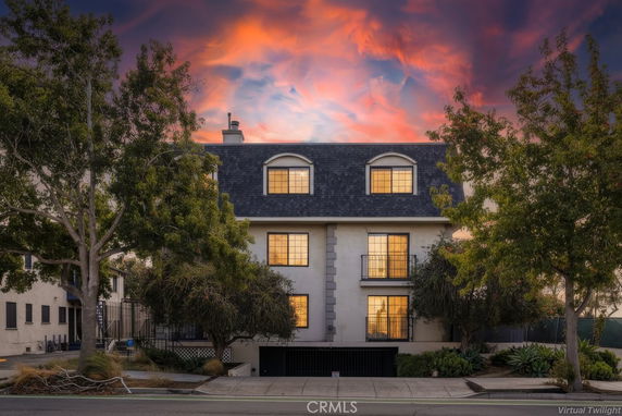 Front view of a multi-story building with a dark roof and illuminated windows, set against a vibrant sunset sky.