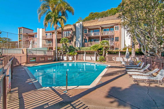 Outdoor swimming pool with sun loungers and a view of a multi-story apartment building.