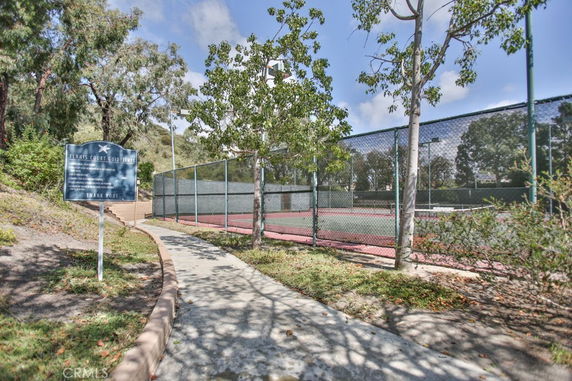 View of a tennis court surrounded by trees and a fenced area.