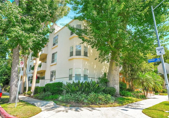 Front view of a multi-story building with balconies and large trees surrounding it.