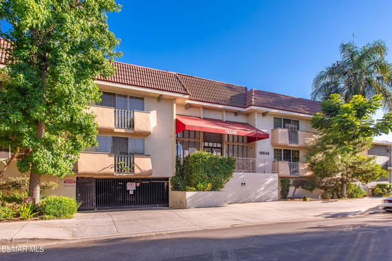 Front view of a multi-story residential building with balconies and a red awning.