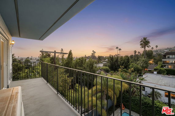 View from a balcony overlooking a lush green landscape with buildings and trees under a twilight sky.