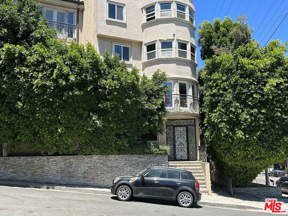 Front view of a multi-story building with curved balconies and large trees in front.