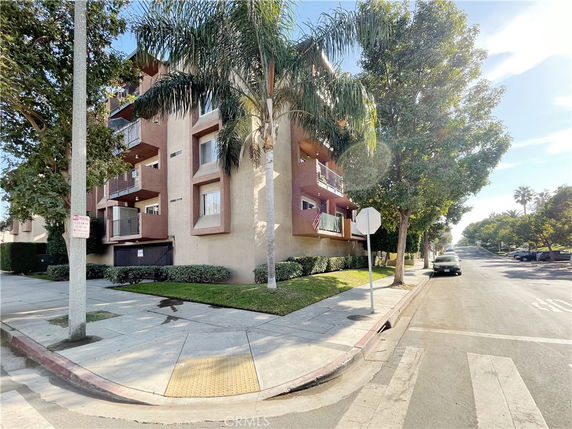 Corner view of an apartment building with multiple balconies and trees lining the street.