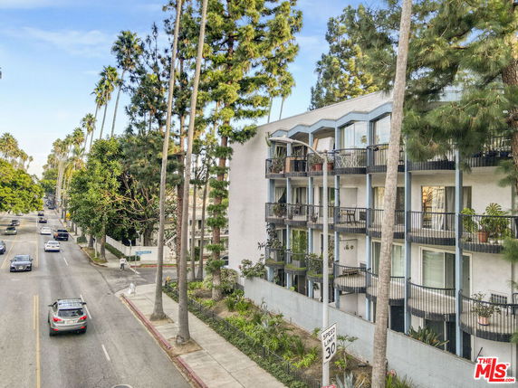Side view of a multi-story apartment building with balconies along a tree-lined street.