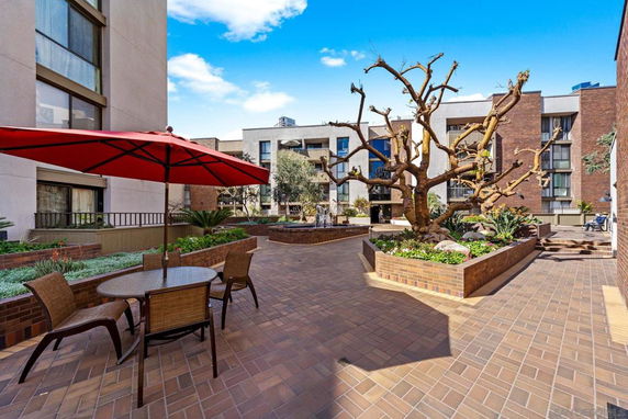 Outdoor courtyard area with brick flooring, surrounded by multi-story buildings and featuring patio furniture with a red umbrella.