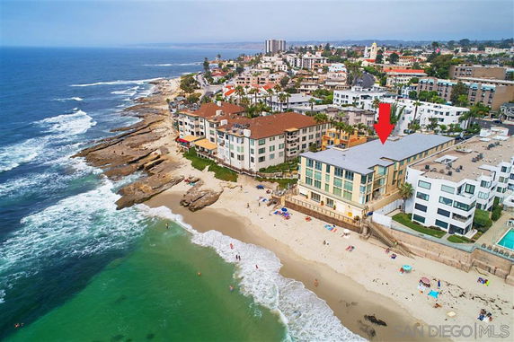 Panoramic view of coastal buildings adjacent to a beach with cliffs and ocean waves.