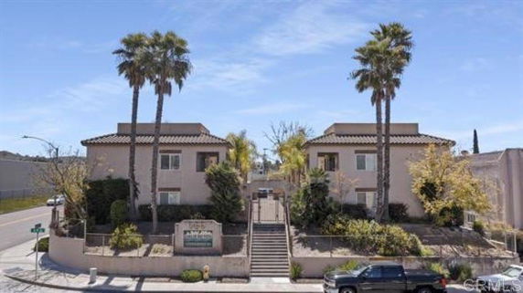 Front view of a two-story apartment building with stairway entrance and palm trees.