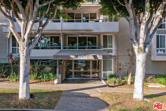 Front view of a multi-story residential building with an entrance canopy and surrounding trees.