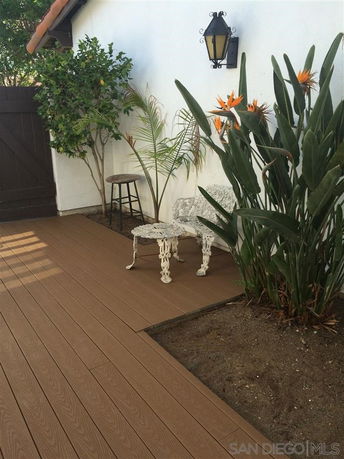 Outdoor patio area with wooden decking, decorative metal chairs, and potted plants.