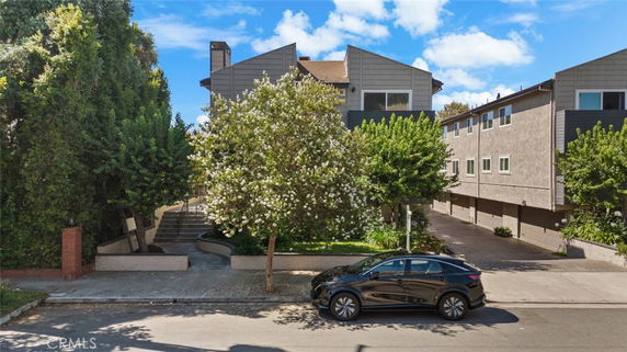Front view of a two-story residential building with trees and a parked car.
