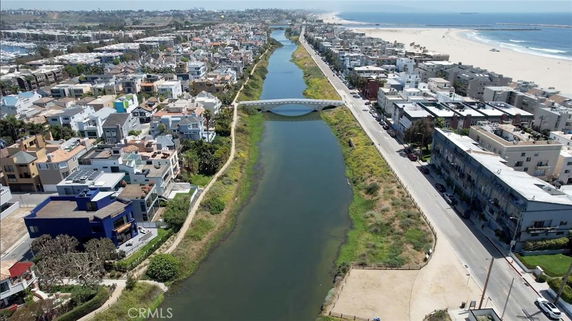 Aerial view of a canal running between residential areas with houses and apartments along the waterway, leading to the beach in the background.