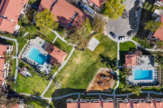 Aerial view of residential area with red-roofed buildings, swimming pools, paths, and green spaces.