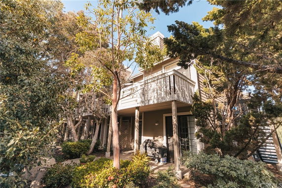 Front view of a two-story house with a balcony surrounded by trees.
